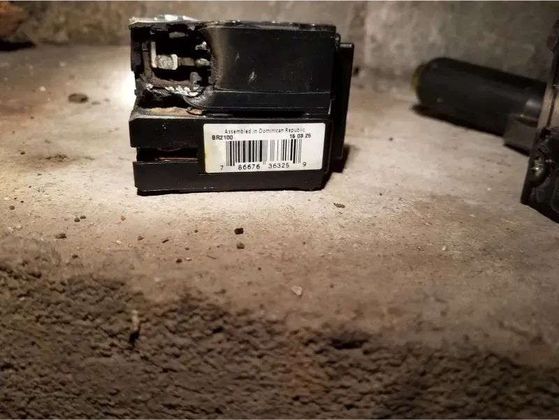 Black electrical box with damaged top and barcode label on a dusty concrete floor.
