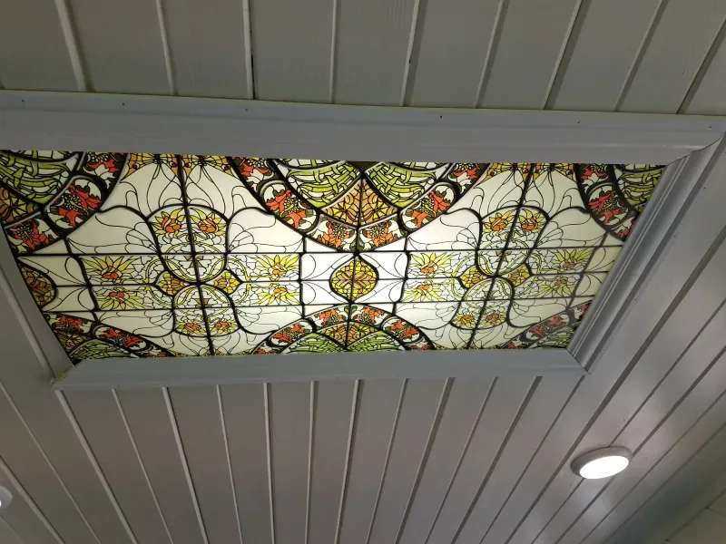 Stained glass ceiling panel with colorful floral and geometric patterns in a white paneled ceiling