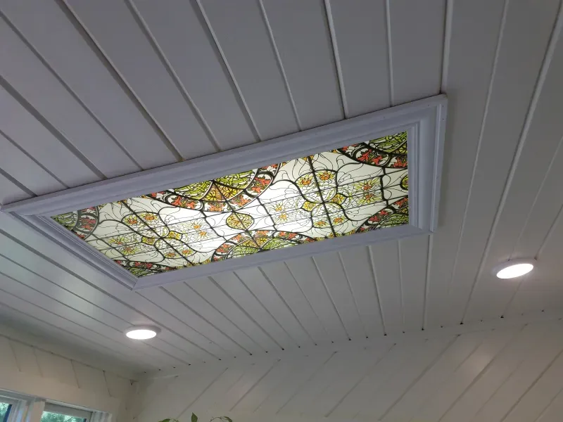 Ceiling skylight with stained-glass panels above white paneled interior ceiling and recessed lights