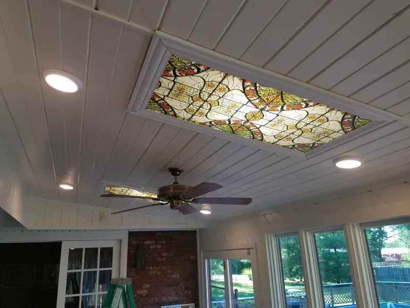 Ceiling with stained-glass skylight, recessed lights, and a ceiling fan in a sunroom.