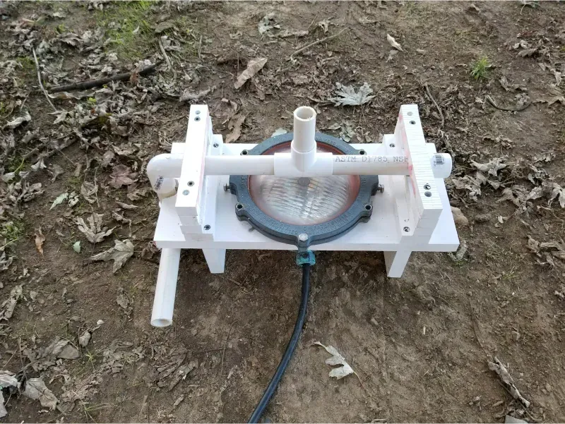 White plastic apparatus with a clear circular center and hose, set on bare ground outdoors
