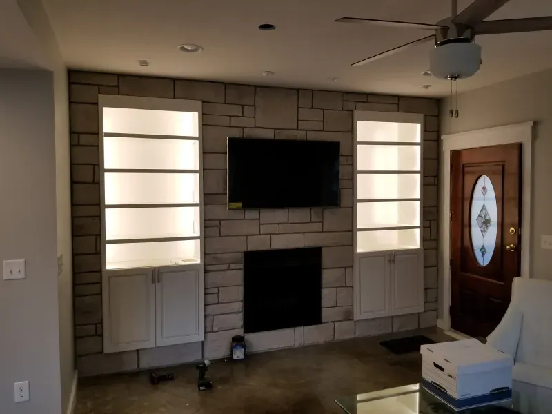 Living room wall with mounted TV, electric fireplace, and two tall window panels over a stone-look backdrop