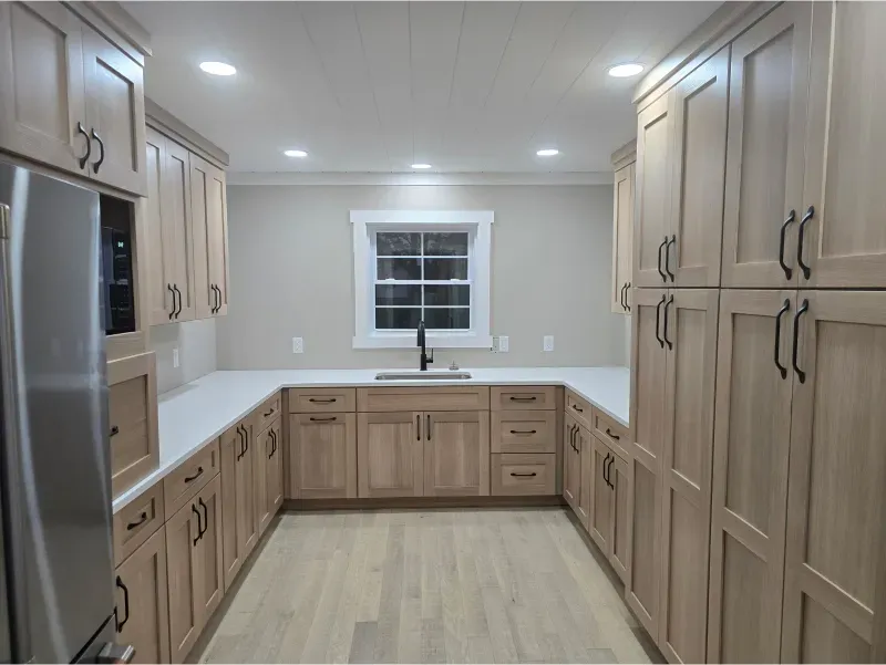 Bright modern kitchen with light wood cabinets, white countertops, and a window over the sink.
