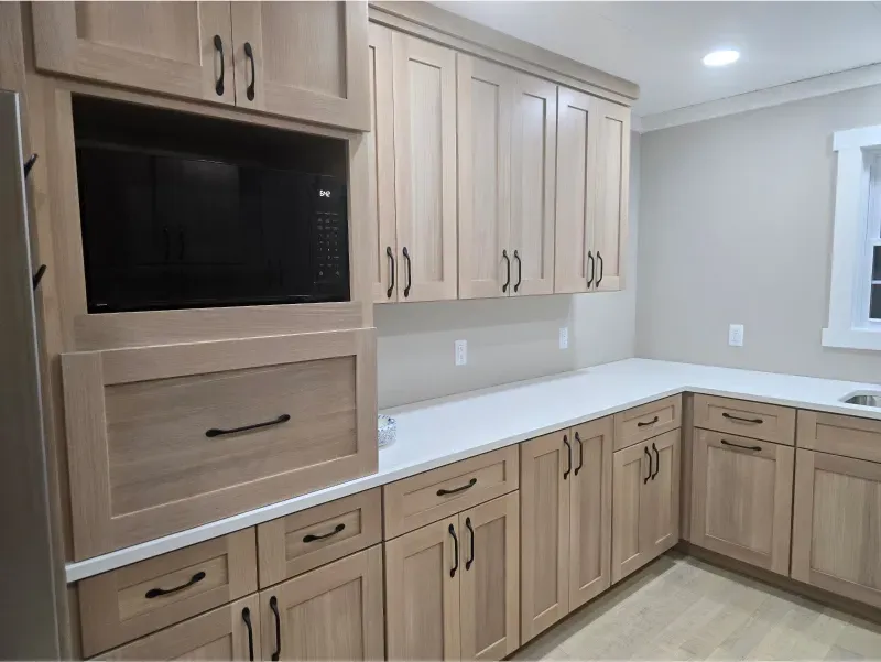 Built-in kitchen cabinets in a light beige and wood finish with a black microwave and white countertop