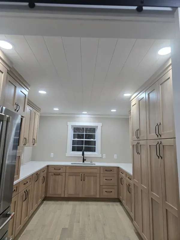 Modern kitchen with light wood cabinets, white countertops, stainless appliances, and a window over the sink