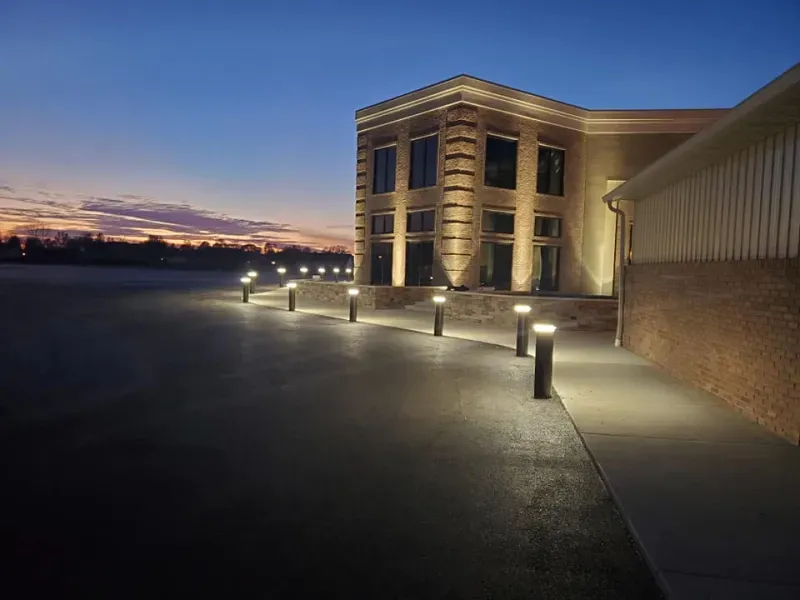 Illuminated building walkway at dusk with bollard lights and a glowing sunset sky
