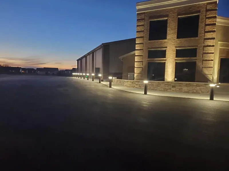 Illuminated stone building at dusk beside an empty paved lot under a blue-orange sky