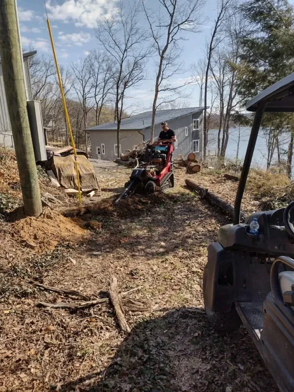 Person on red ATV in a wooded yard near a house, with a pickup truck in the foreground