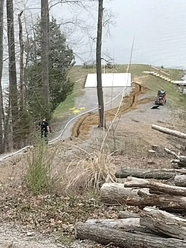 Two cyclists on a dirt trail beside a wooded slope and a white-roofed shelter