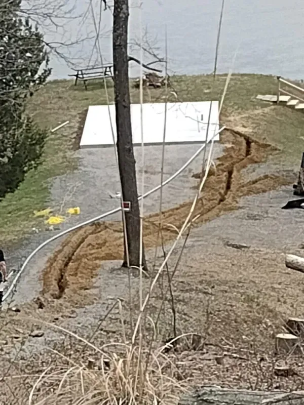 Damaged roadside slope with a deep erosion gully, exposed soil, and a utility pole near a concrete slab