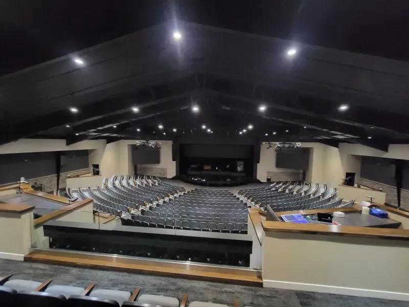 Empty auditorium with rows of seats under a dark peaked ceiling, viewed from the balcony.
