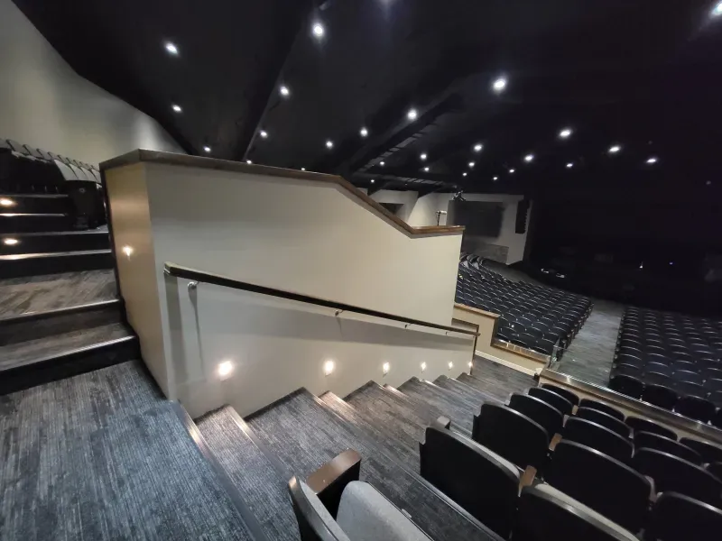 Empty modern auditorium with tiered seating, stage steps, and recessed ceiling lights