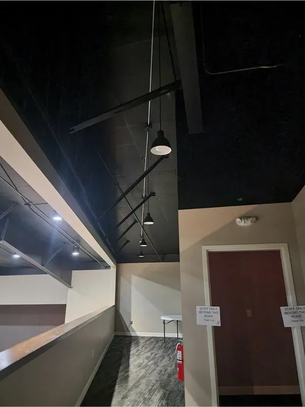 Dim hallway with exposed black ceiling, hanging lights, white walls, and two brown doors.