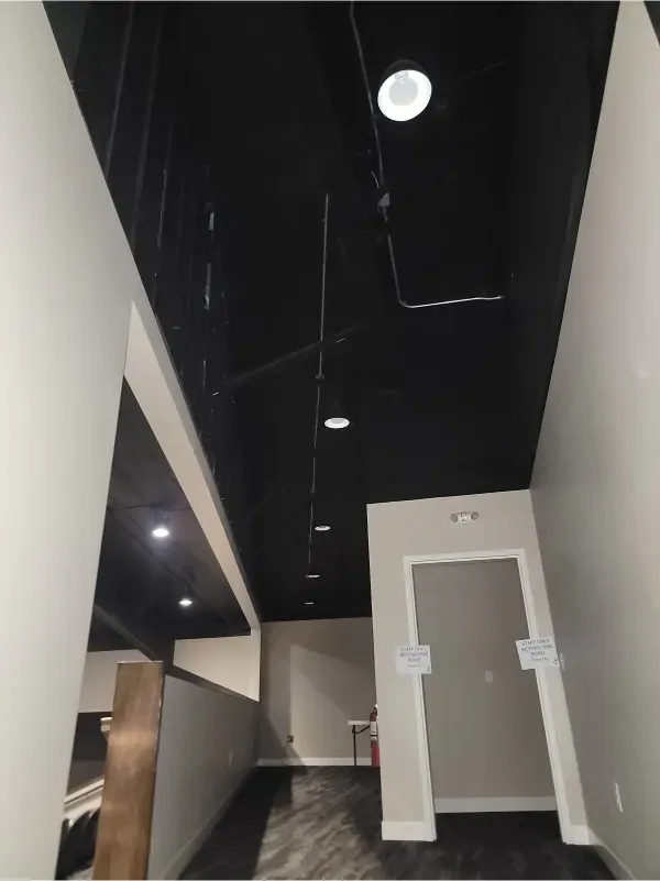 Hallway with black ceiling, white walls, recessed lights, and a restroom door at the end