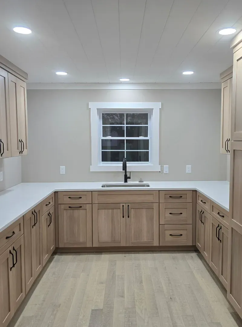 Bright kitchen with light wood cabinets, white countertops, and a window above the sink.