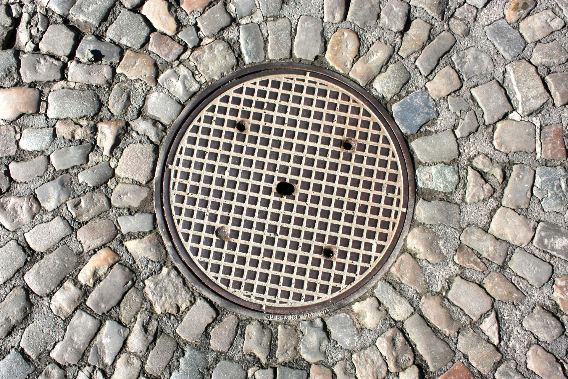 Plaque d'égout centrée dans un pavage en pavés.