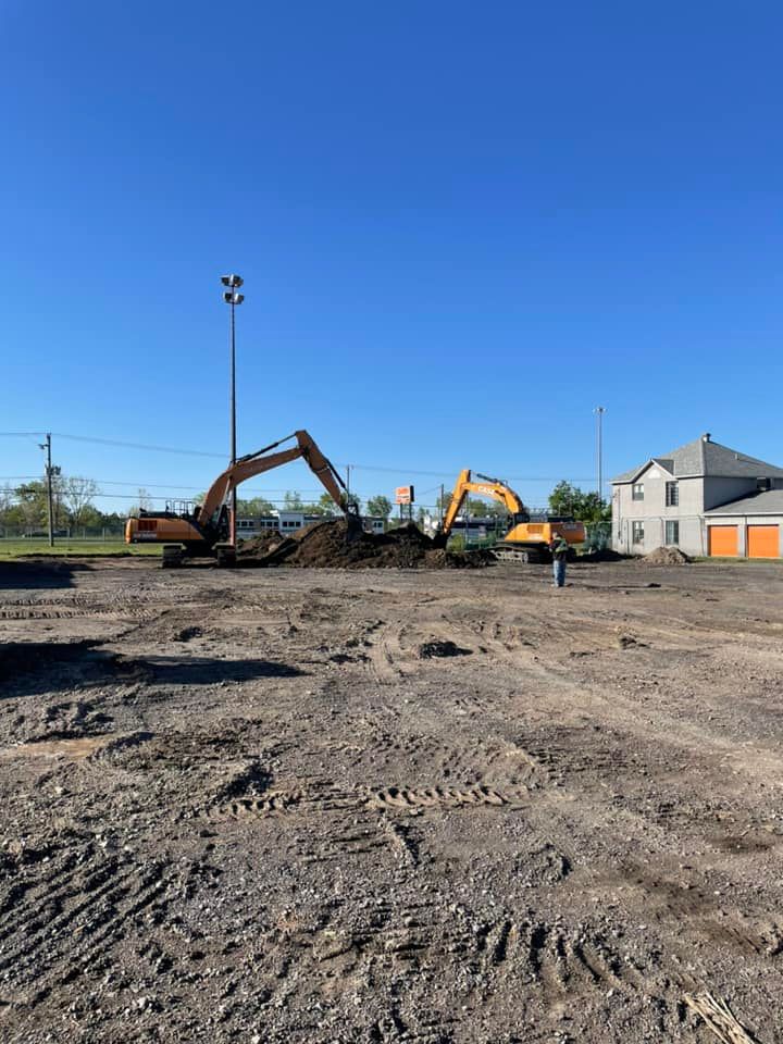 Deux excavatrices creusent la terre sur un chantier de construction sous un ciel bleu dégagé.