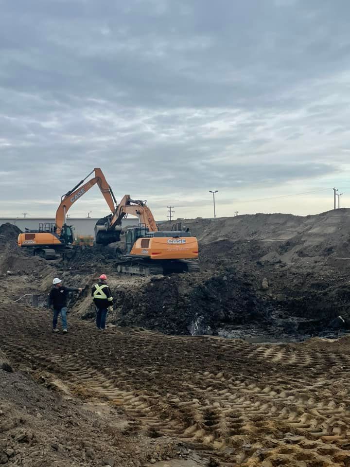 Deux excavatrices et deux ouvriers sur un chantier, sous un ciel nuageux.