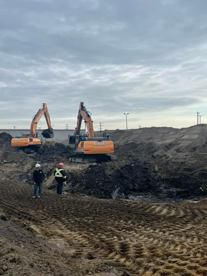 Deux pelleteuses orange sur un chantier ; deux ouvriers se tiennent à proximité. Ciel nuageux.