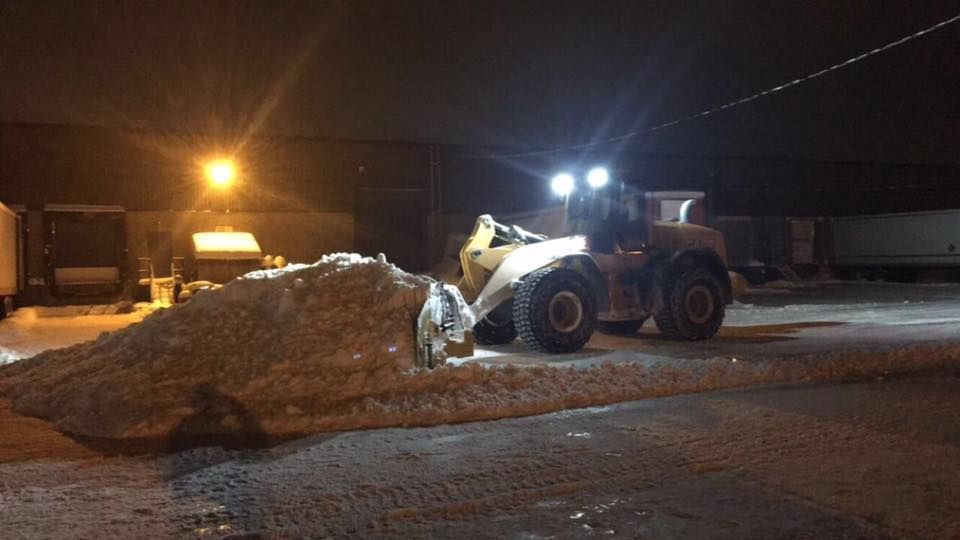 Chargeuse sur pneus déneigeant de nuit, éclairée par des phares et des lampadaires.