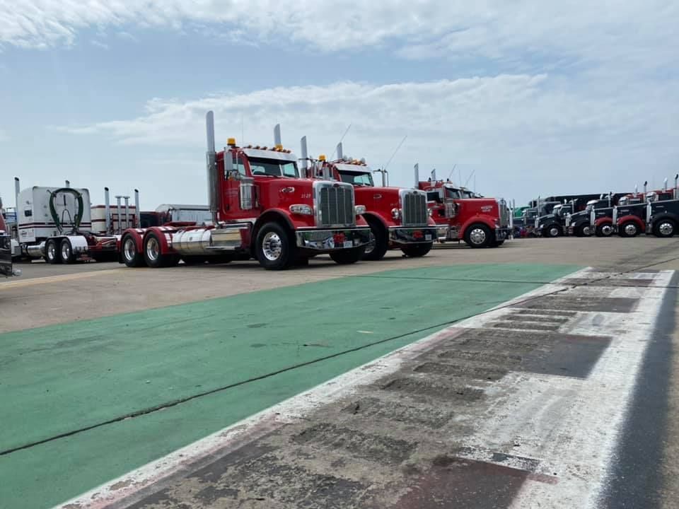 Des semi-remorques rouges sont stationnées sur un parking par une journée ensoleillée. D'autres camions sont visibles à l'arrière-plan.