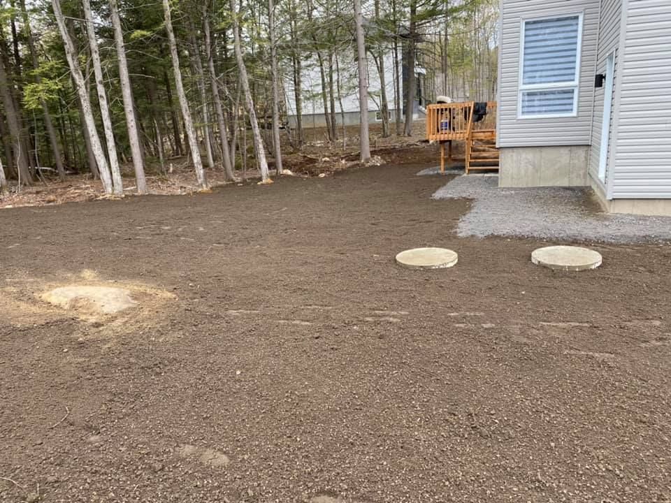 Jardin avec terreau foncé fraîchement étalé ; maison à droite, terrasse en arrière-plan, arbres à gauche.