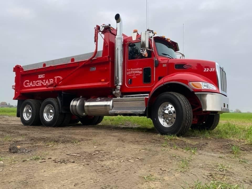 Camion-benne rouge avec le logo « Gaighard » sur un chemin de terre, ciel couvert.
