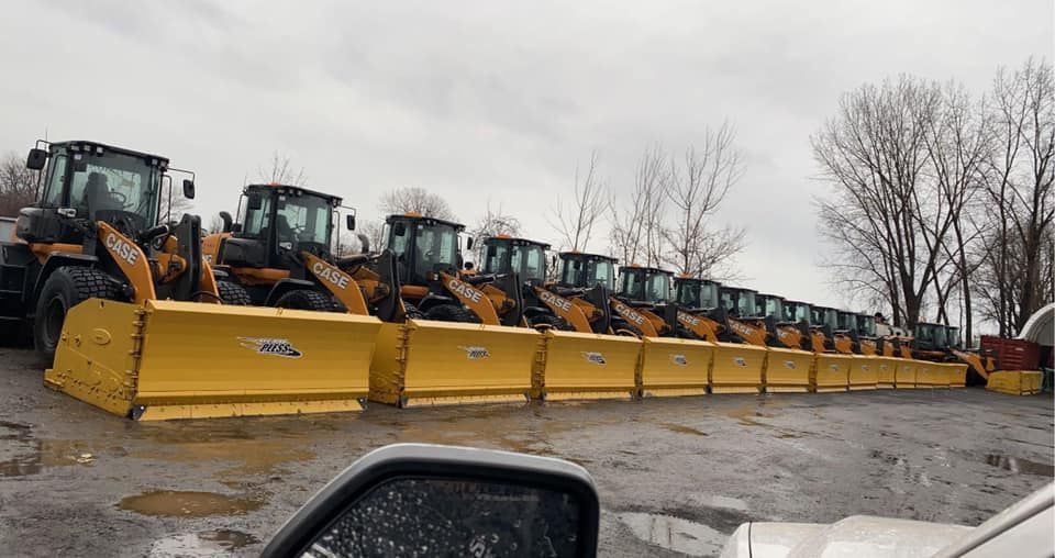 Une rangée de chasse-neige jaunes, attelés à des chargeuses frontales, alignés par temps nuageux.