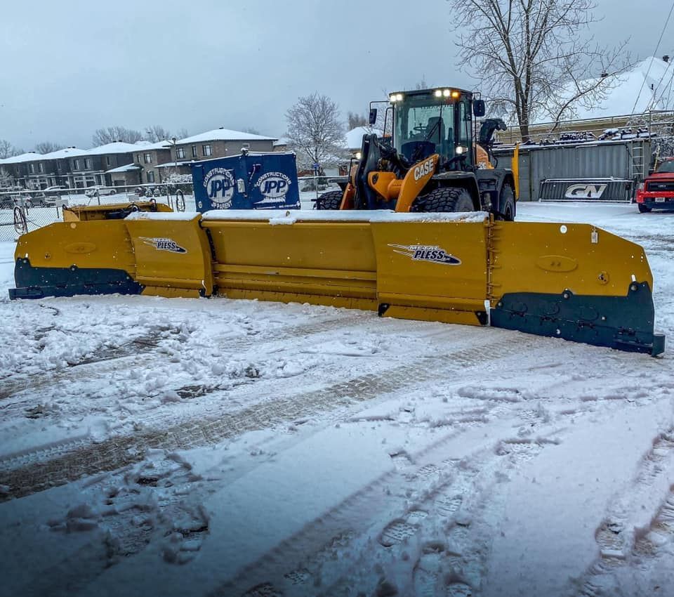 Une déneigeuse jaune dégage la neige d'un parking par temps nuageux.