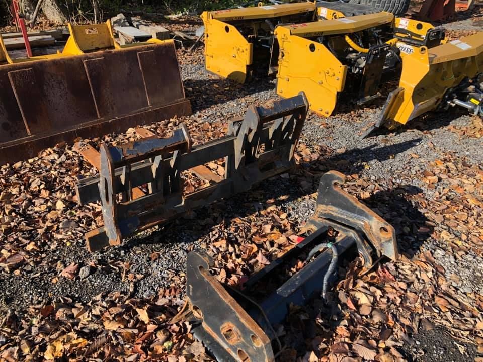Plusieurs souffleuses à neige jaunes et leurs accessoires sont entreposés à l'extérieur. Un accessoire noir se trouve au premier plan.