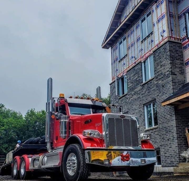 A bright red semi-truck parked next to a multi-story building under construction with exposed wood framing and stone brick.