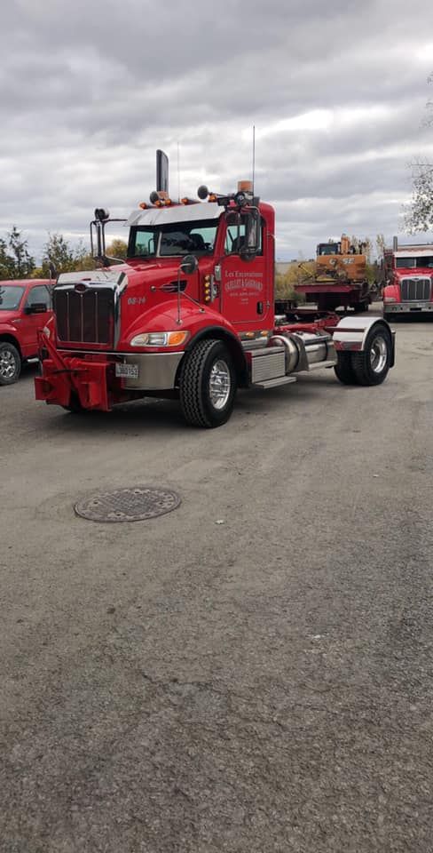Un semi-remorque rouge est stationné sur l'asphalte d'un parking sous un ciel nuageux.