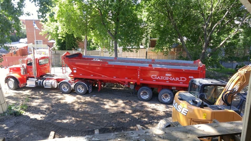 Un camion-benne rouge tractant une remorque rouge sur un chantier de construction.