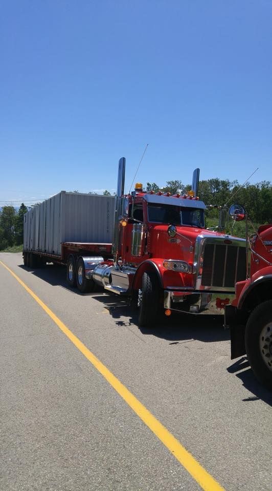 Un semi-remorque rouge transportant des blocs de béton gris empilés sur une remorque est stationné en bordure de route par une journée ensoleillée.