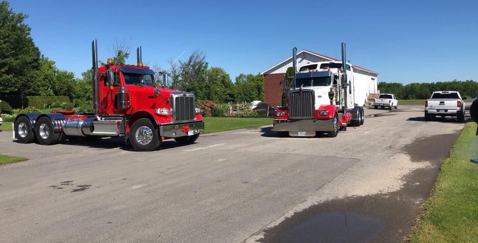 Deux semi-remorques, l'une rouge, l'autre blanche, roulent sur une route goudronnée par une journée ensoleillée.