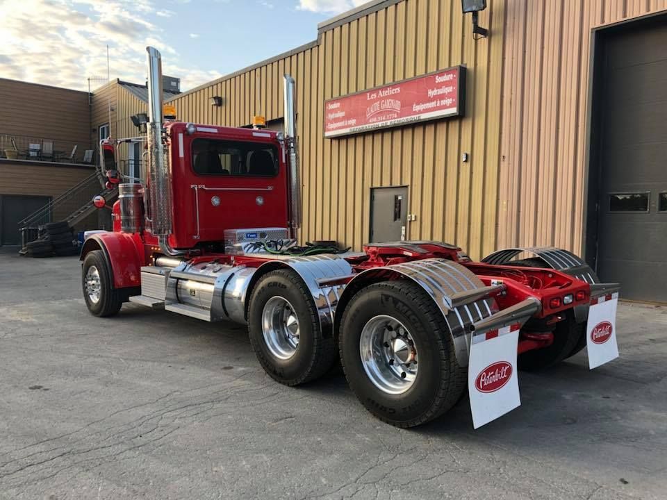 Un semi-remorque Peterbilt rouge est garé devant un bâtiment beige avec des accents chromés.