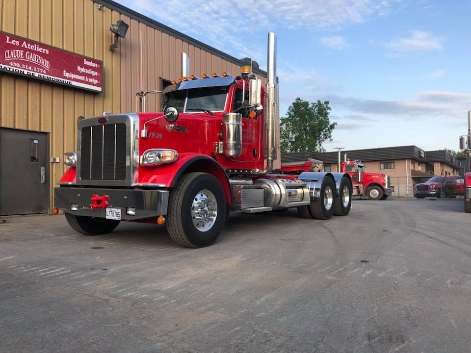 Un semi-remorque Peterbilt rouge est stationné devant un bâtiment avec une enseigne, en journée.