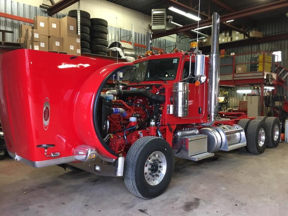 Un semi-remorque rouge, capot ouvert, laisse apparaître le moteur. À l'intérieur d'un garage.