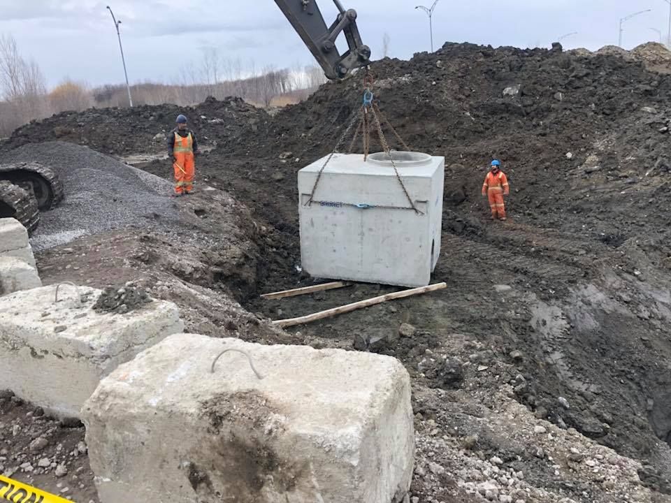 Des ouvriers installent un bloc de béton sur un chantier. Une excavatrice soulève le bloc.
