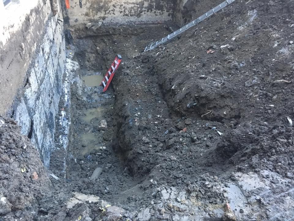 Chantier de construction excavé, sol boueux et niveau rouge appuyé contre le mur.