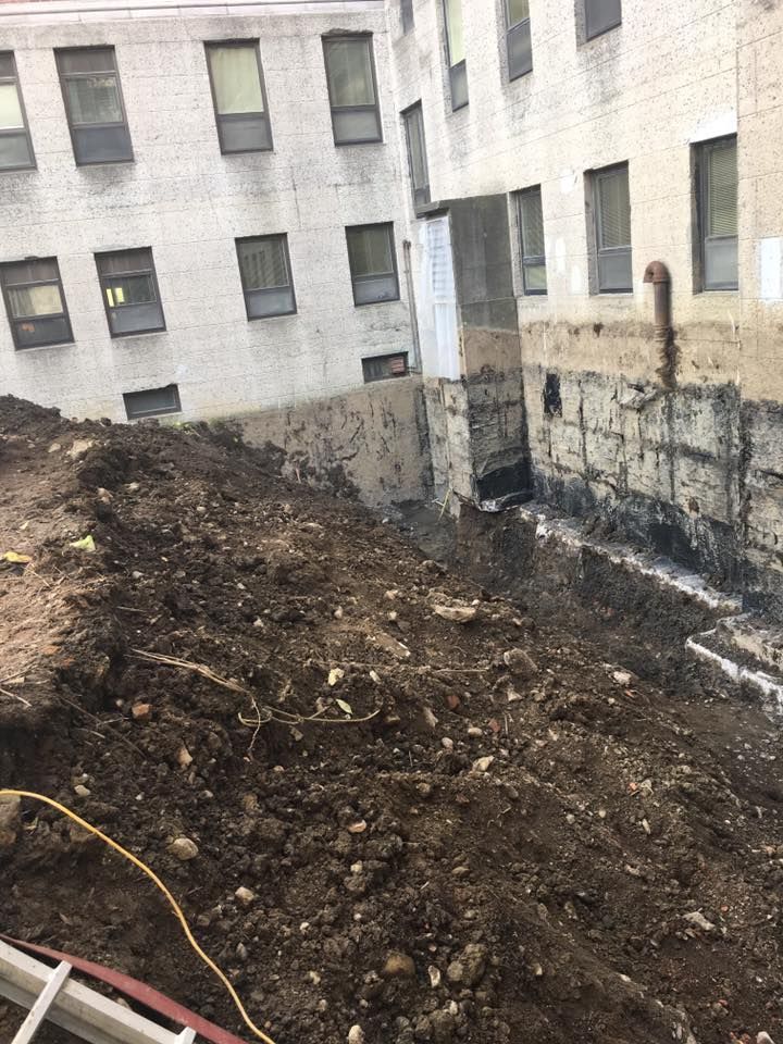 Site de fouilles comprenant un bâtiment, des fondations visibles et un grand tas de terre.