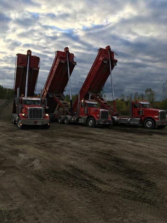 Trois camions-bennes rouges à benne surélevée, sur un terrain en terre.