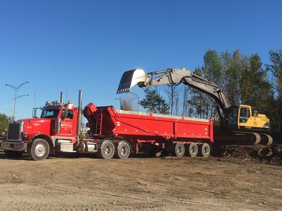 Un camion-benne rouge est chargé par une excavatrice jaune sur un chantier de construction.