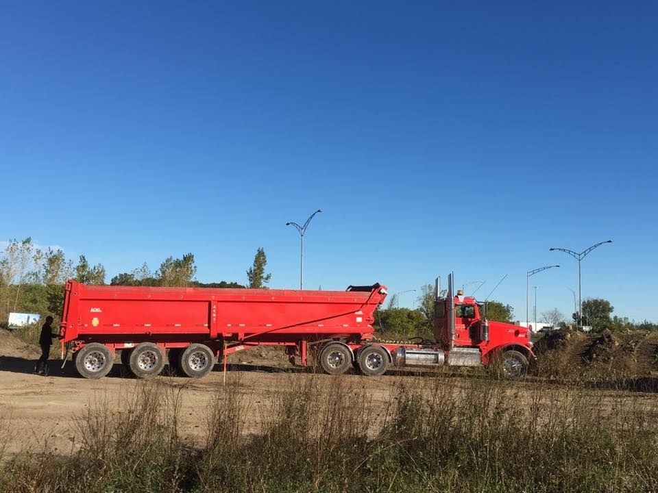 Un camion-benne rouge sur un chemin de terre sous un ciel bleu clair.