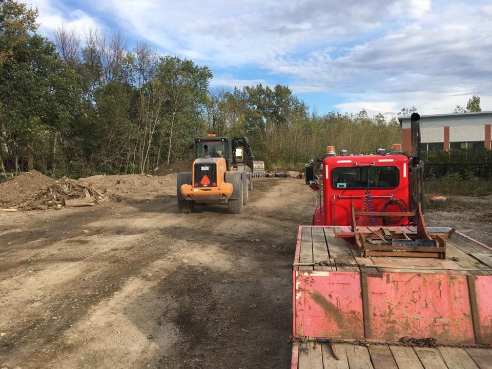 Chargeuse frontale et camion rouge sur un chemin de terre, arbres en arrière-plan, ciel couvert.