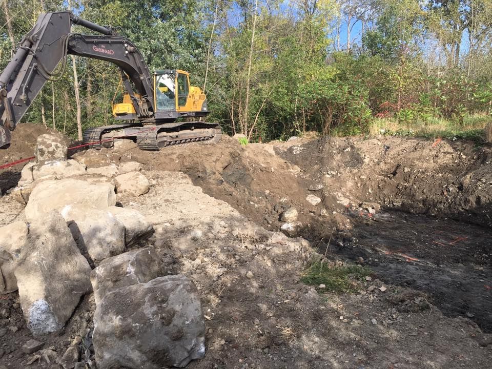Une excavatrice sur un tas de terre, déplaçant des roches près des arbres.