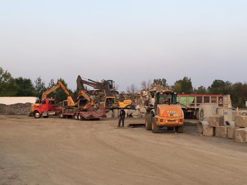 Engins de chantier lourds sur un site de dépôt de pierres : camions, excavatrices et chargeuses.