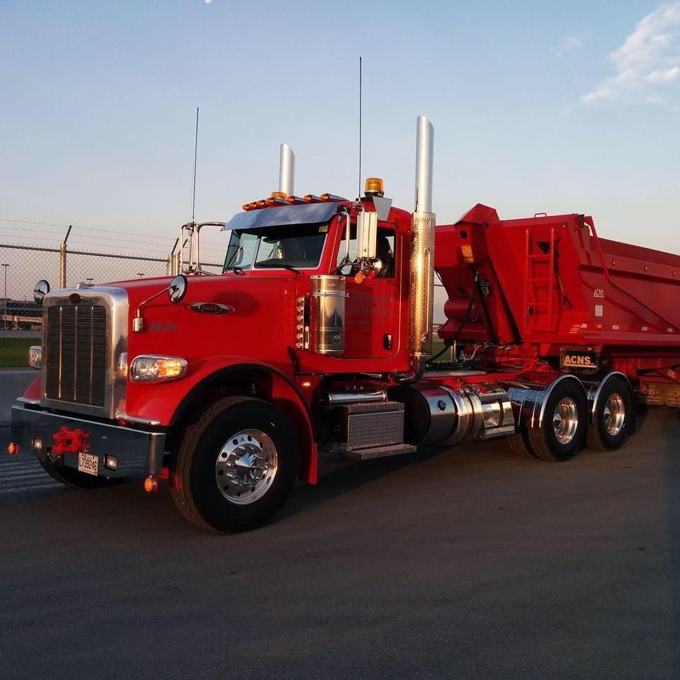 Un semi-remorque Peterbilt rouge avec une benne basculante est stationné sur le bitume, en extérieur.
