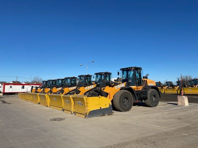 Line of CASE wheel loaders with yellow snow plows, parked under a blue sky.
