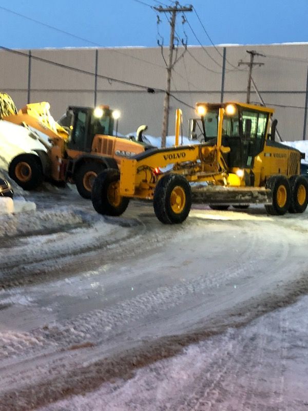 Yellow Volvo snow grader and loader clearing a snowy lot.